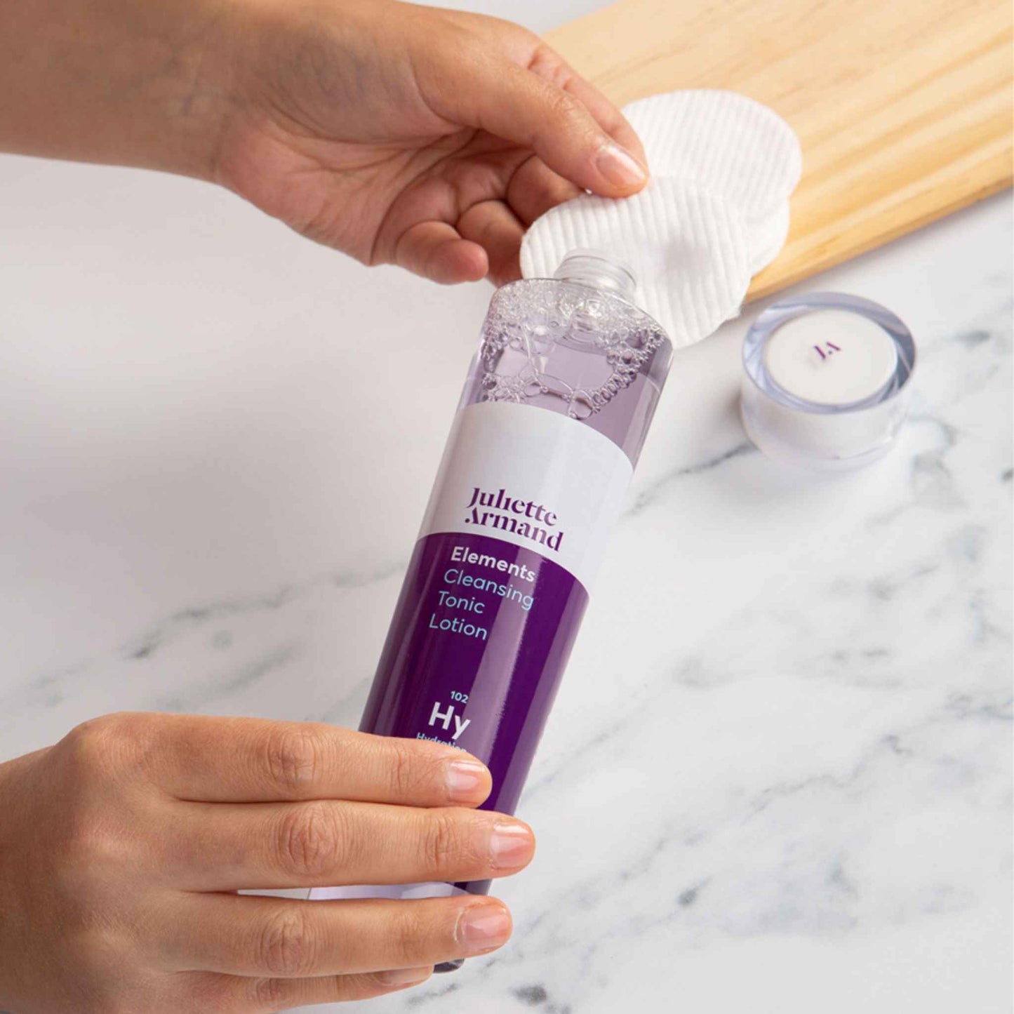 Person holding a bottle of Juliette Armand cleansing tonic lotion with a white cloth.