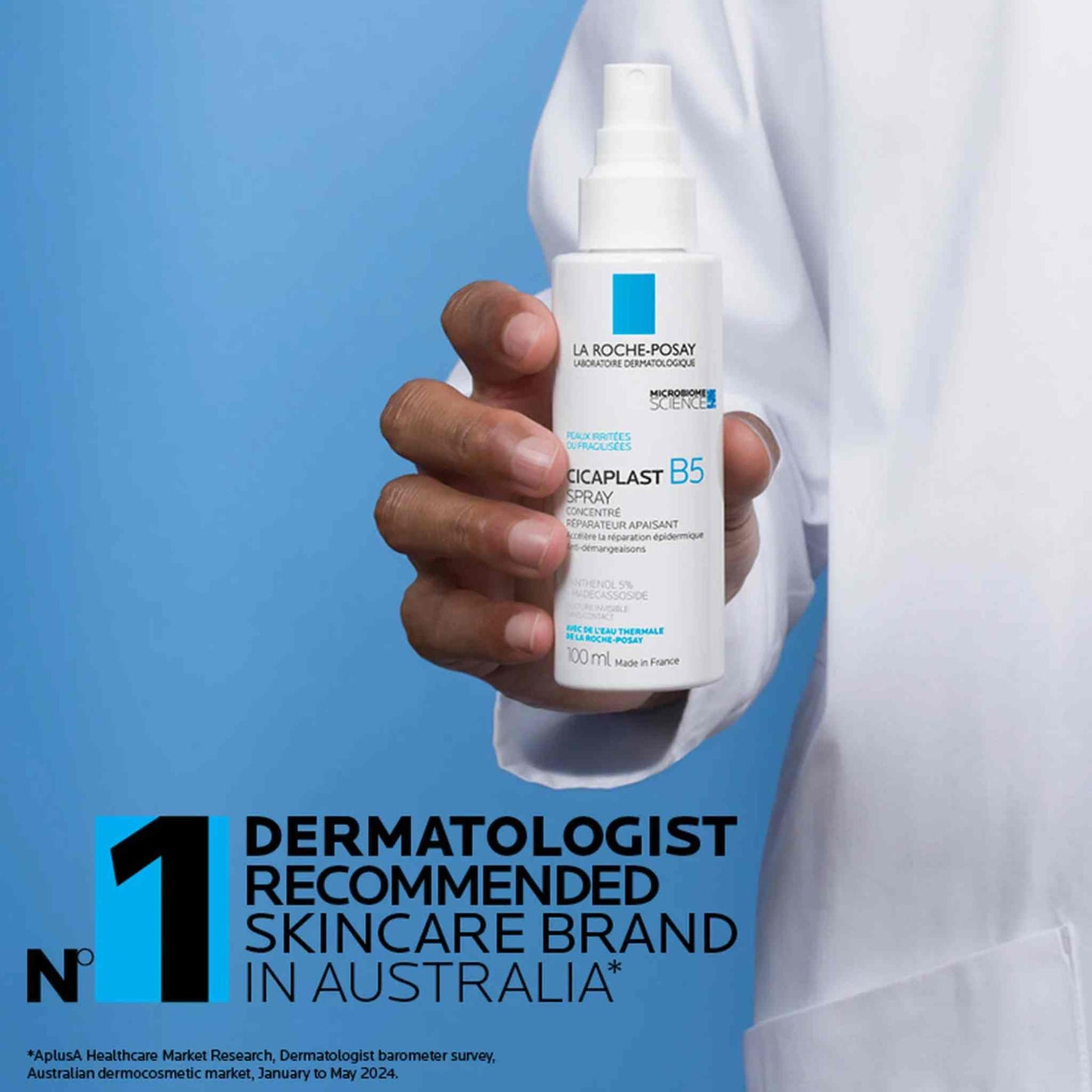 A hand in a white lab coat holds a bottle of La Roche-Posay Cicaplast B5 spray 100mL  against a blue background with promotional text at the bottom.
