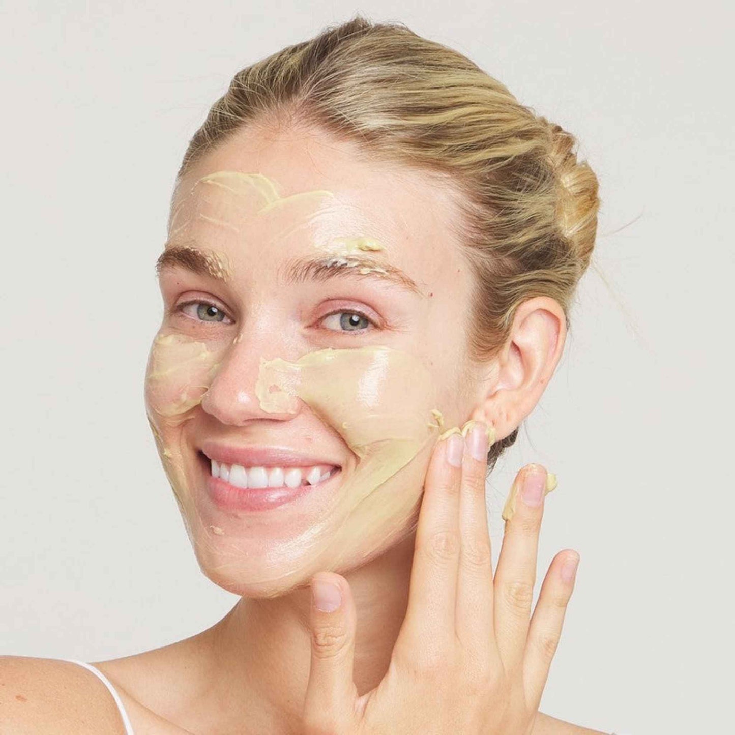 Woman applying a Skin Zyme Mask with a white background