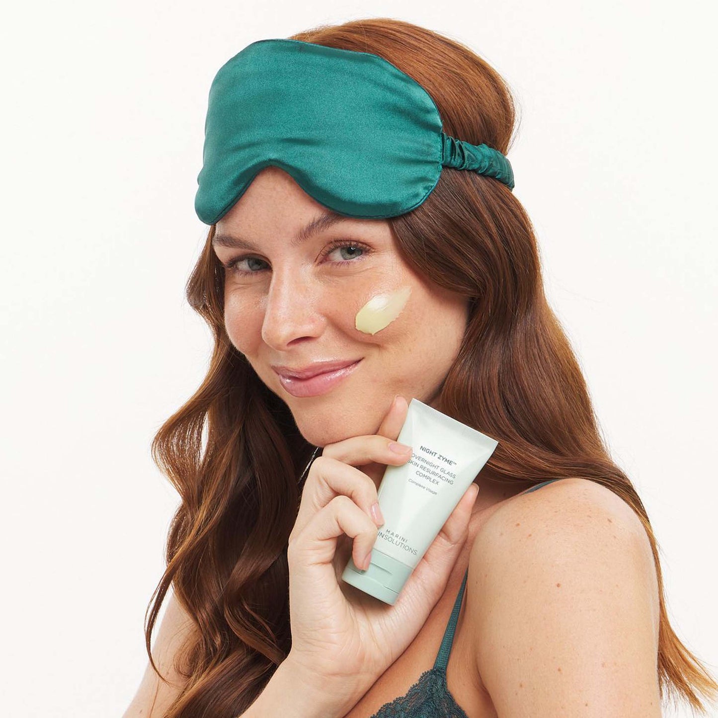 Woman applying Marini SkinSolutions Night Zyme to her face with a green sleep mask on a white background